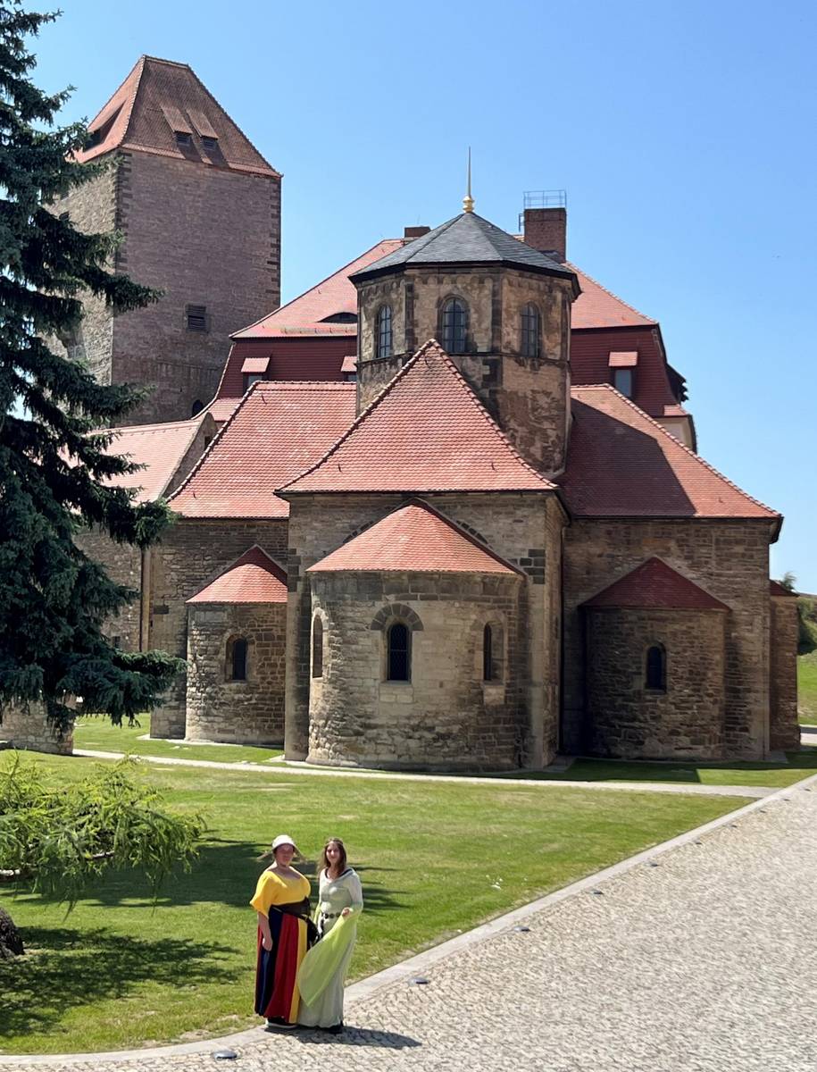 Zwei Frauen im mittelalterlichen Gewändern stehen vor einer Kirche